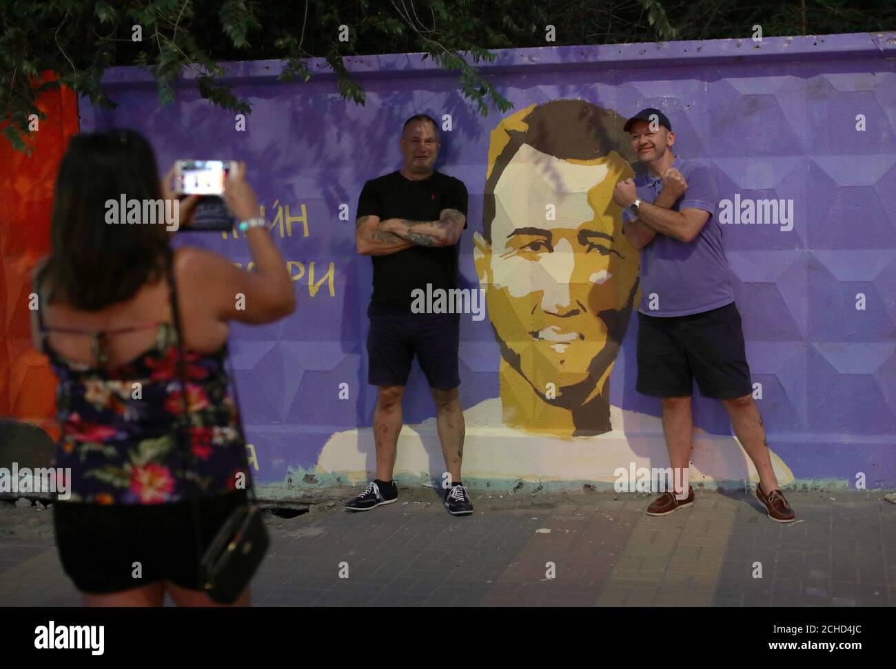 Due uomini posa per una foto da un murale di Inghilterra del Harry Kane con parole re Harry scritto in russo vicino al fan fest centro di Volgograd davanti al suo compagno di squadra la partita di apertura del 2018 FIFA World Cup in Russia. Foto Stock