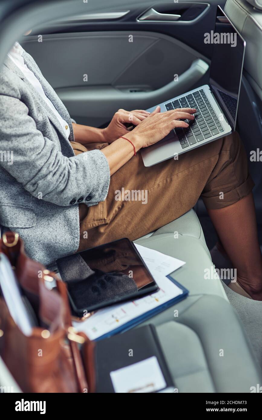 Lavorando online in taxi, foto verticale di donna d'affari utilizzando il computer portatile mentre si siede sul sedile posteriore in auto Foto Stock