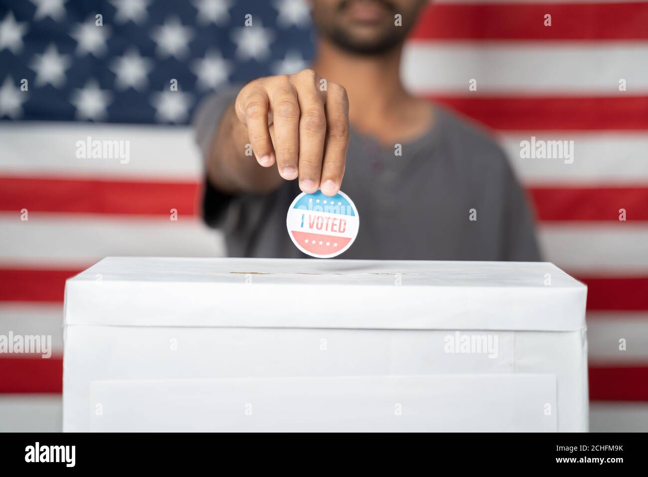 Concetto di elezioni USA, primo piano di mani mettendo ho votato adesivo all'interno della casella di voto con la bandiera degli Stati Uniti come sfondo. Foto Stock