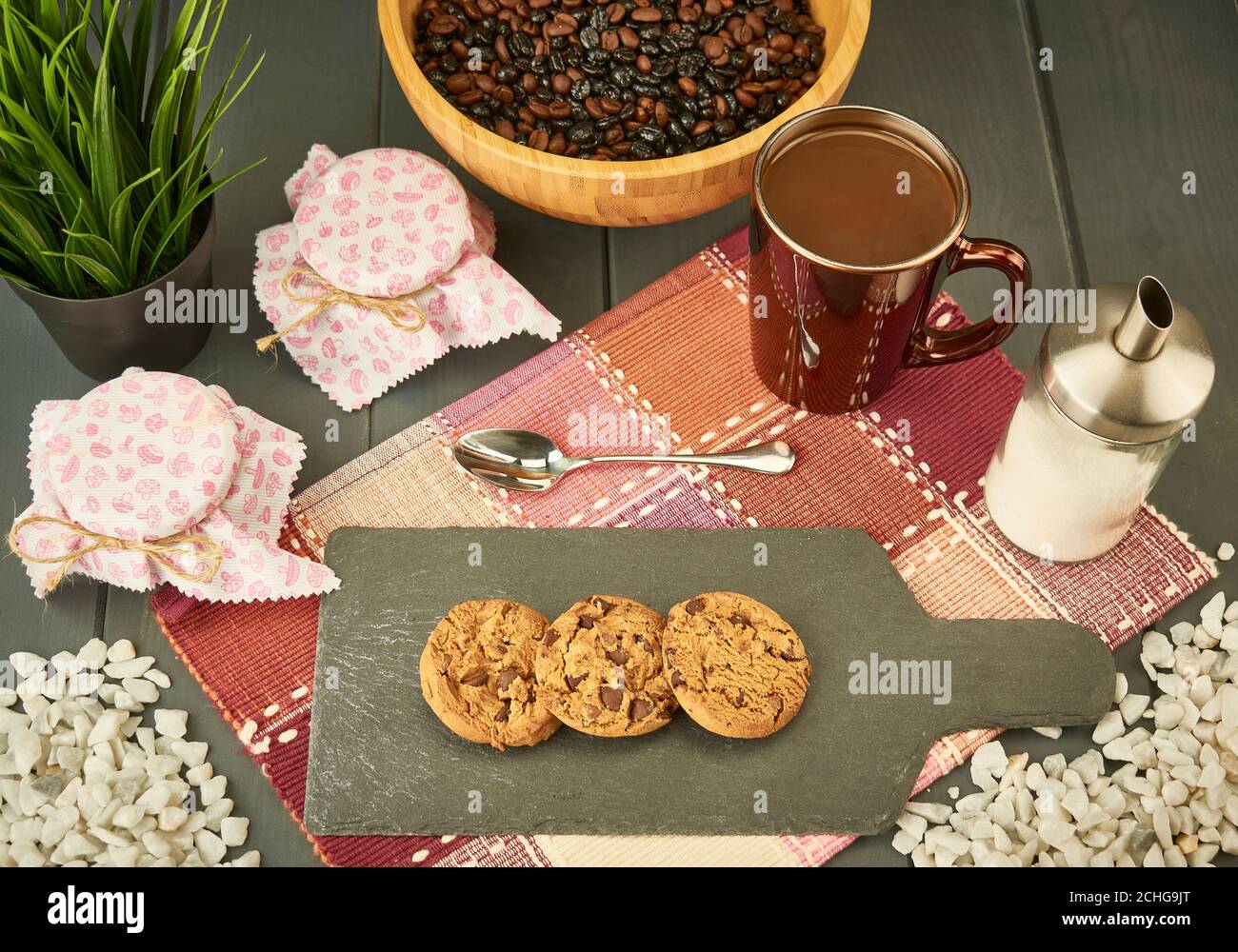 Biscotti al cioccolato su una tavola di ardesia, con miele, una tazza di caffè, un cucchiaio, zucchero e una ciotola con una miscela di caffè naturale e torrefatto su una ta di legno Foto Stock