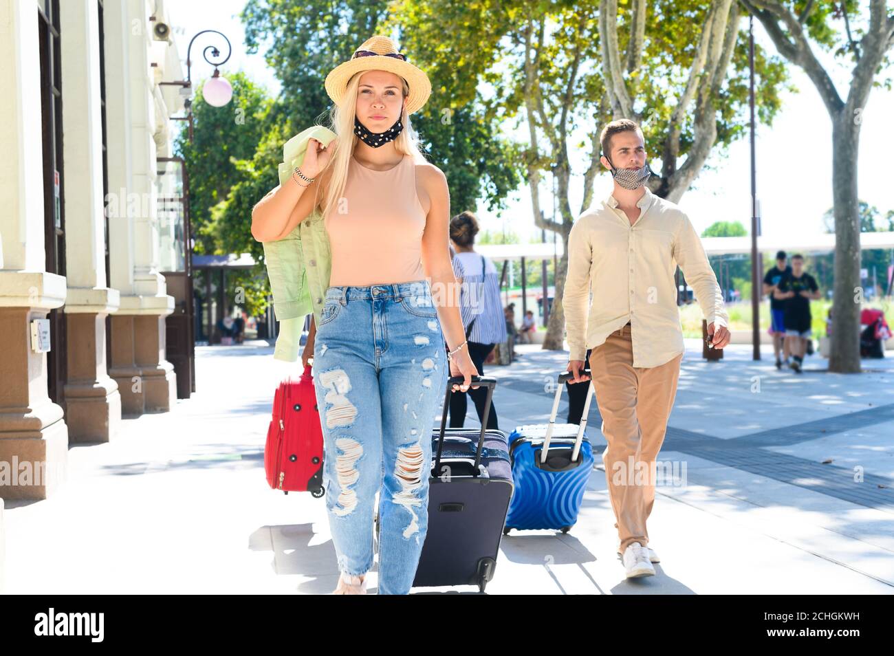 Pretti ragazza e ragazzo che camminano di fronte al treno Stazione con la maschera - due passeggiate con i bagagli - nuovo concetto di viaggio normale e stile di vita Foto Stock