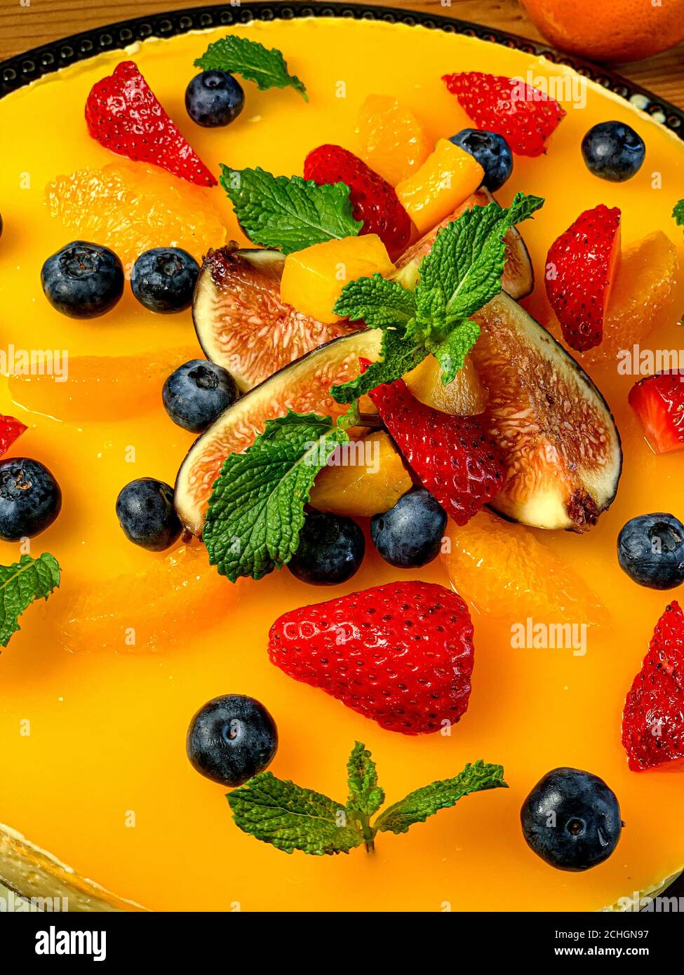 Deliziosa cheesecake arancione decorata con frutta e foglie di menta Foto Stock