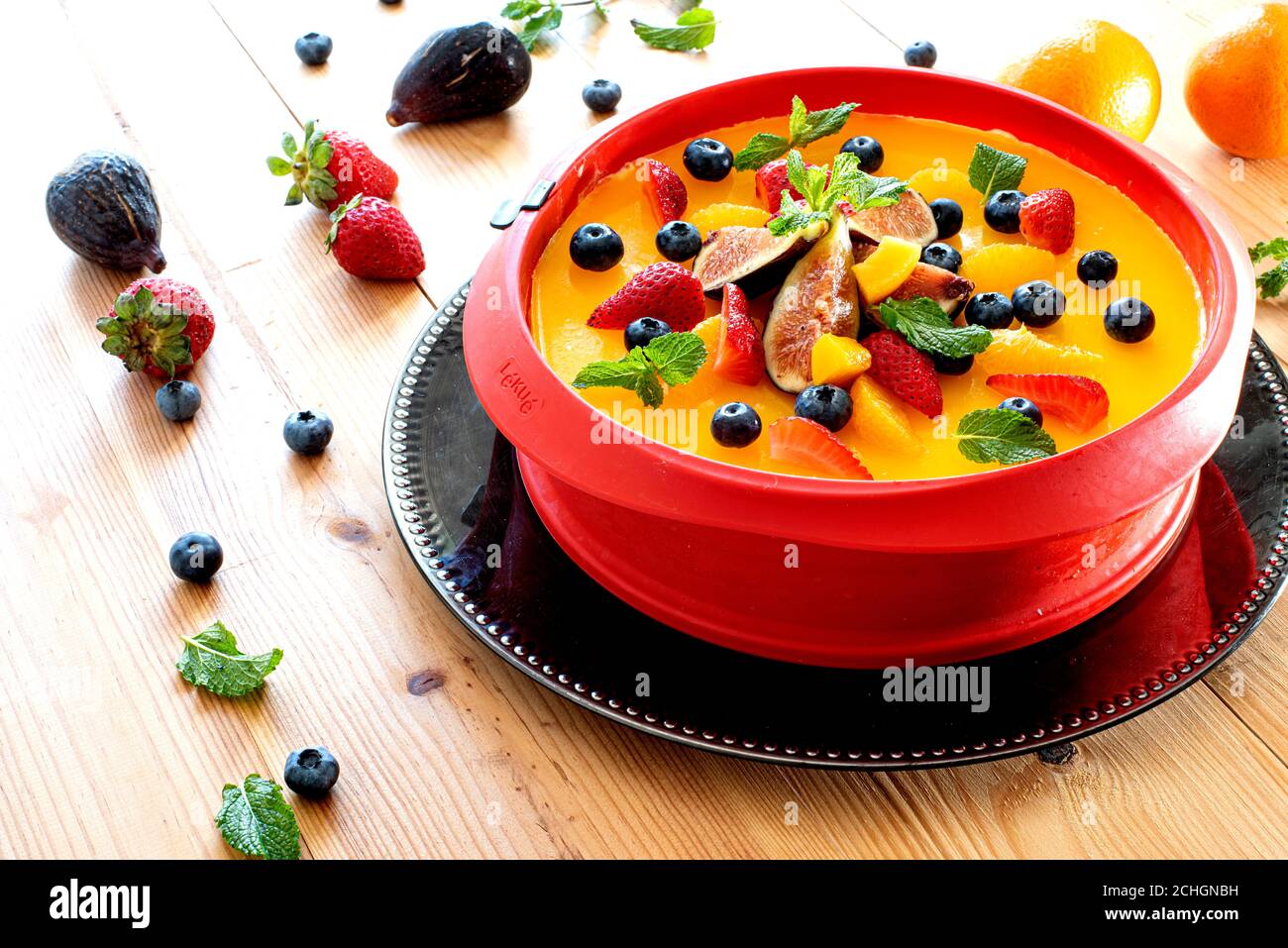 Deliziosa cheesecake arancione decorata con frutta e foglie di menta Foto Stock
