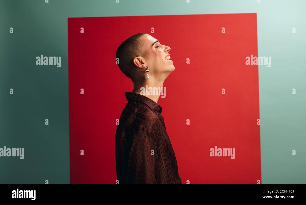 Vista del profilo di un uomo transgender che indossa orecchini e trucco sorridente. Uomo gay che guarda felice. Foto Stock