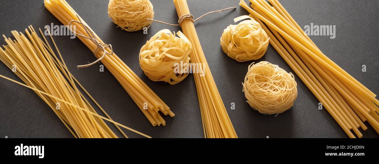 Concetto di cucina della pasta. Spaghetti e tagliatelle di pasta cruda su sfondo nero, vista closeup, striscione Foto Stock