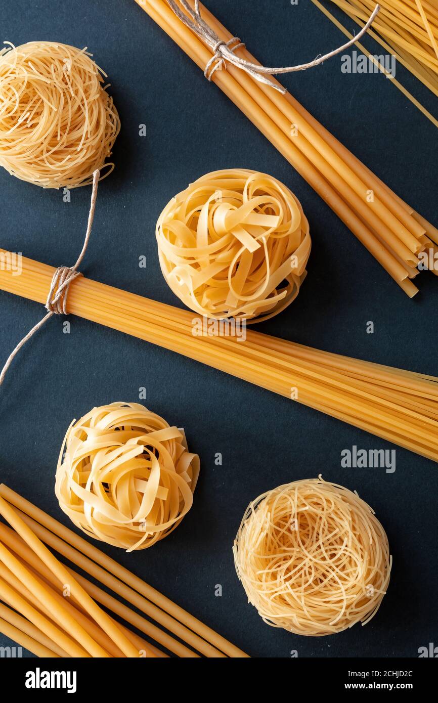 Concetto di cucina della pasta. Spaghetti e tagliatelle di pasta cruda su sfondo nero, vista dall'alto, verticale Foto Stock