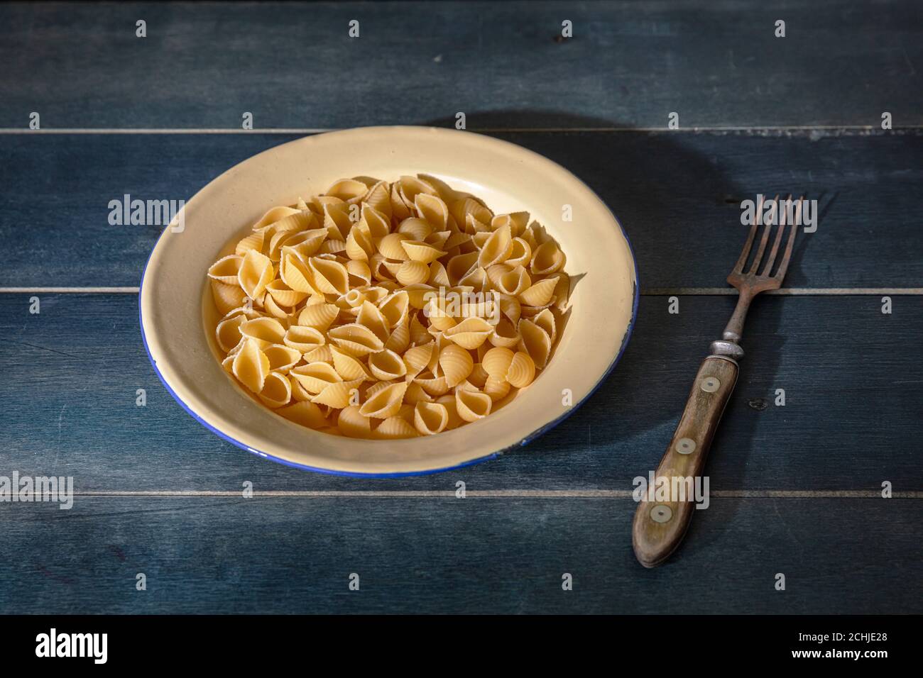 Concetto di cucina della pasta. Pasta fresca fatta in casa a forma di conchiglia servita in un piatto su sfondo di legno blu, vista closeup Foto Stock