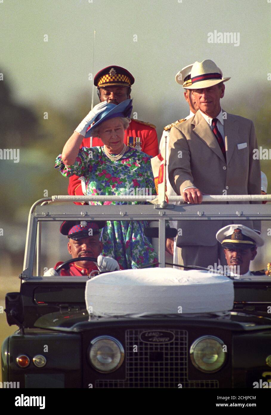 La regina Elisabetta II tiene sul suo cappello mentre lei ed il duca di  Edinburgo cavalcano in una Land Rover di cima aperta mentre ispezionano i  membri del secondo battaglione del reggimento