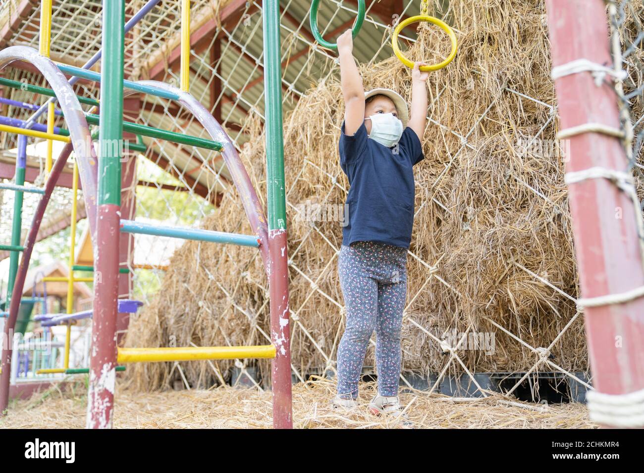 Bambina asiatica che indossa una maschera chirurgica per prevenire la diffusione di raffreddore e influenza e virus. Si divertono e si divertono nel parco giochi all'aperto. Foto Stock