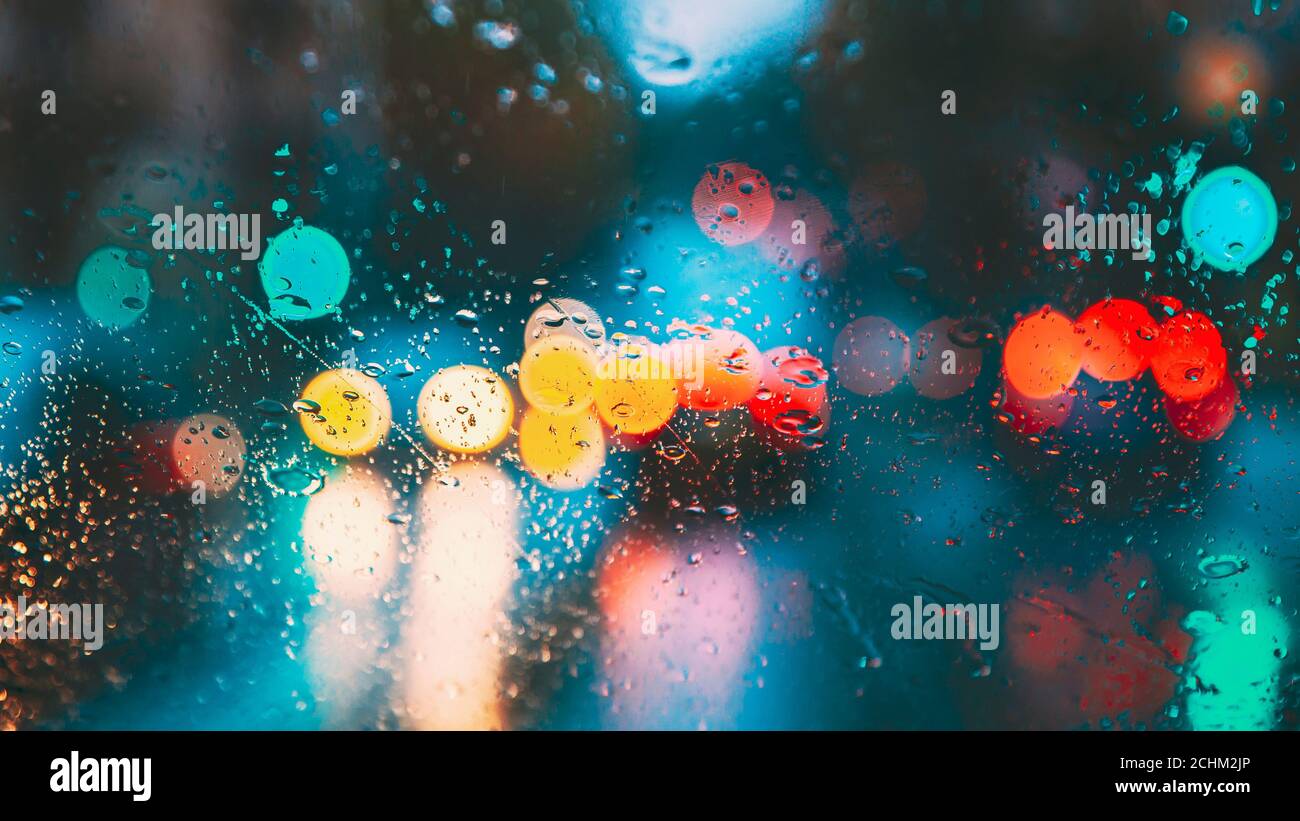 Gocce di acqua di pioggia nella notte o sera le luci di strada sul vetro azzurro sfondo. Street Bokeh Lights Out di messa a fuoco. Autunno sfondo astratto Foto Stock