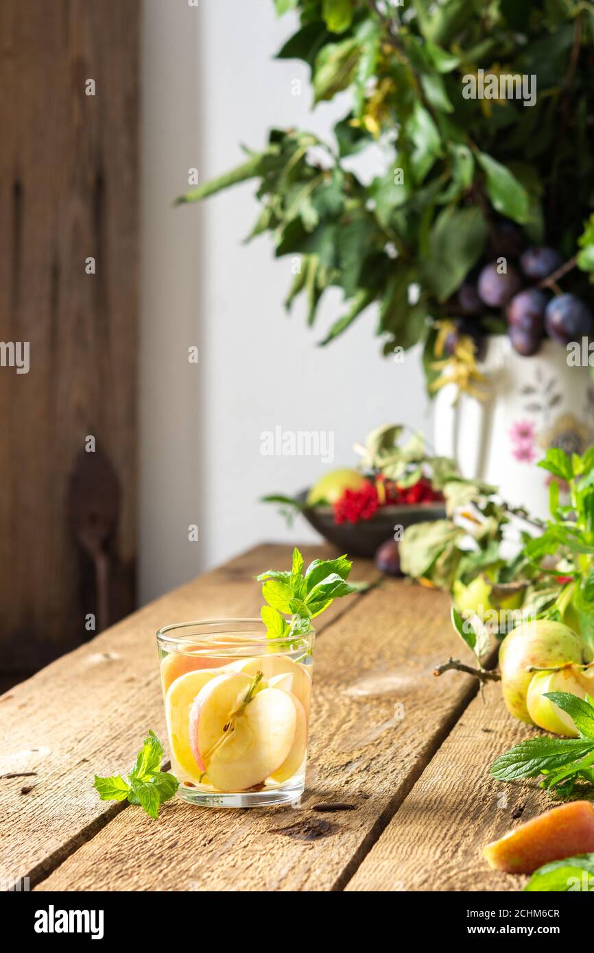 Mela d'autunno, fette di mela con succo e menta in un bicchiere su un tavolo di legno, foglie in un vaso, mattina nel villaggio, concetto rustico Foto Stock