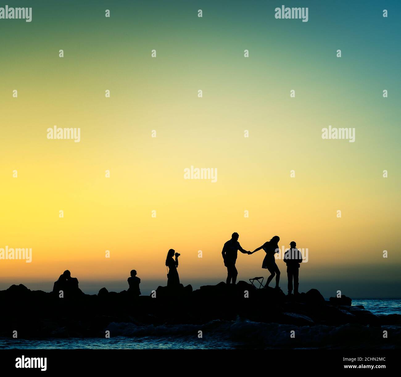 varie persone al tramonto sulla costa rocciosa Foto Stock