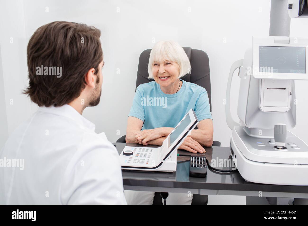 Sorridente donna anziana ha una consultazione con il suo optometrist per un controllo dell'occhio-su. Se una donna ha una vista povera, il medico darà una prescrizione per Foto Stock