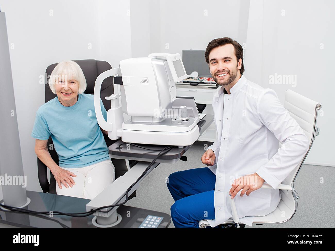 Un optoetrist sorridente con il suo paziente anziano, amichevole-guardare la macchina fotografica, controllo dell'occhio. Esame visivo e diagnostica visiva Foto Stock