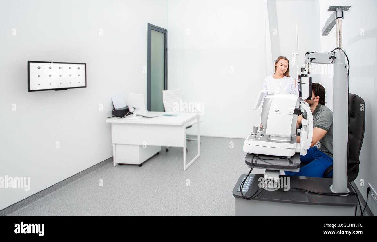 donna oftalmologista con un paziente umano vicino ad apparecchiature oftalmiche in un moderno ufficio oftalmologico. Diagnostica degli occhi Foto Stock