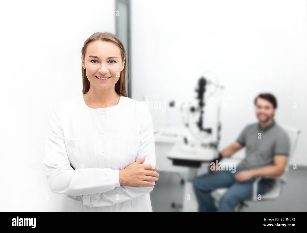 Ritratto di una bella donna oftalmologista in un moderno ufficio oftalmologico, sullo sfondo un bel paziente maschile è seduto Foto Stock