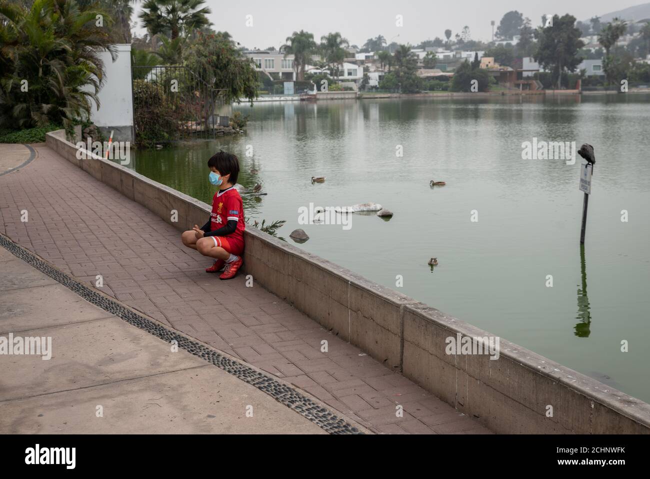 Ragazzo che indossa una maschera facciale e un vestito sportivo accanto a un lago a Lima, Perú Foto Stock