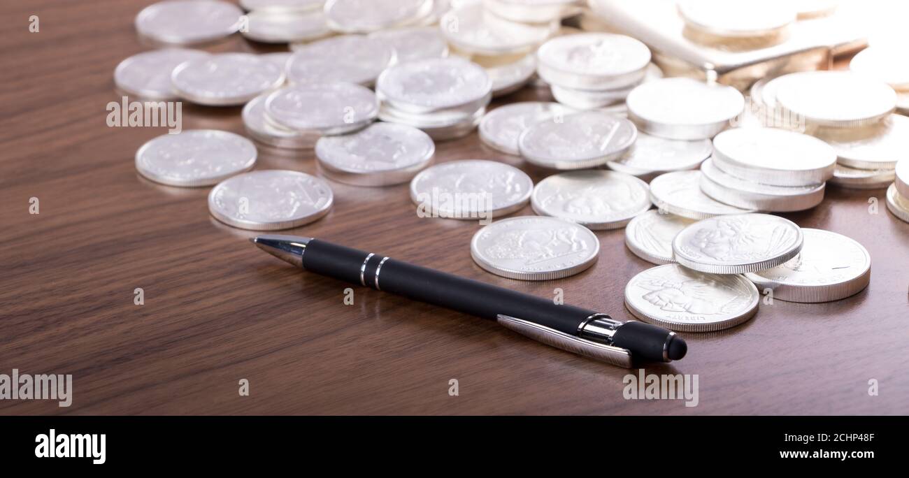 Closeup di monete d'argento sparse su un tavolo di legno con una penna. Concetto di conteggio/investimento Foto Stock