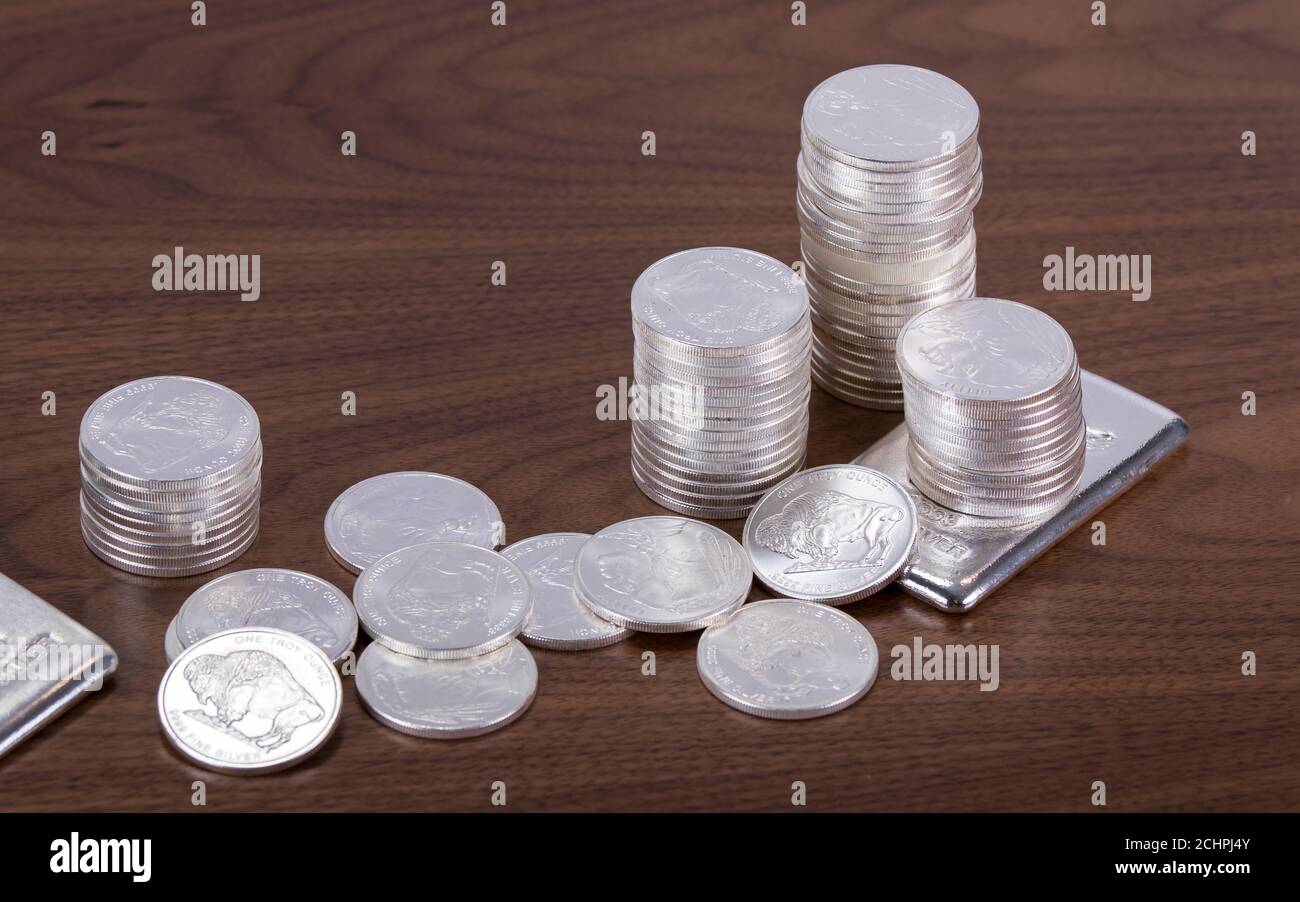 Closeup di barrette d'argento e monete sparse su un legno tabella Foto Stock