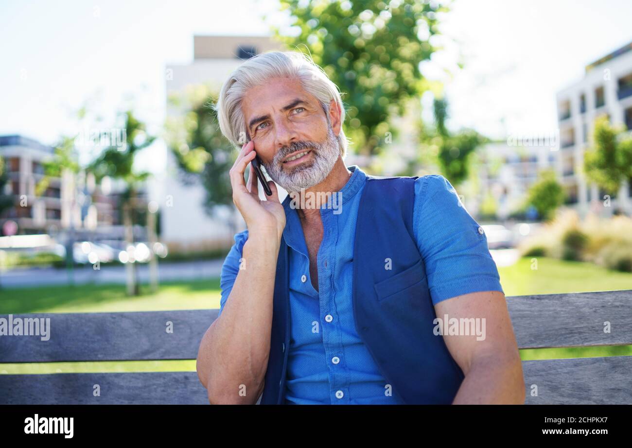 Ritratto di un uomo maturo seduto all'aperto in città, utilizzando uno smartphone. Foto Stock