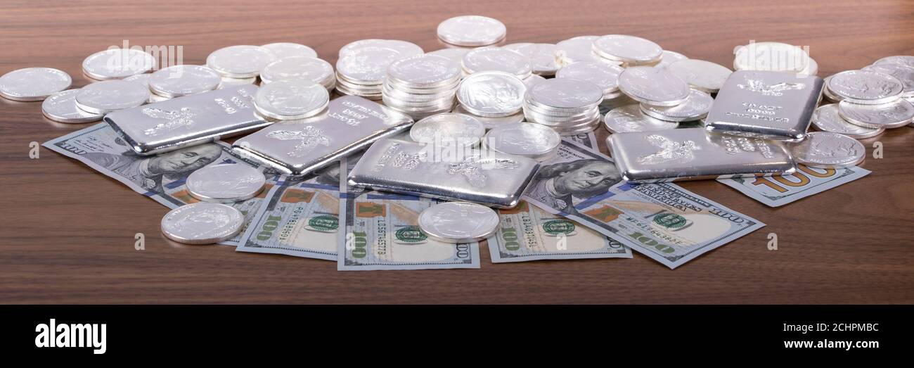 Closeup di barrette d'argento e monete d'argento e 100 dollari bollette su tavolo di legno Foto Stock