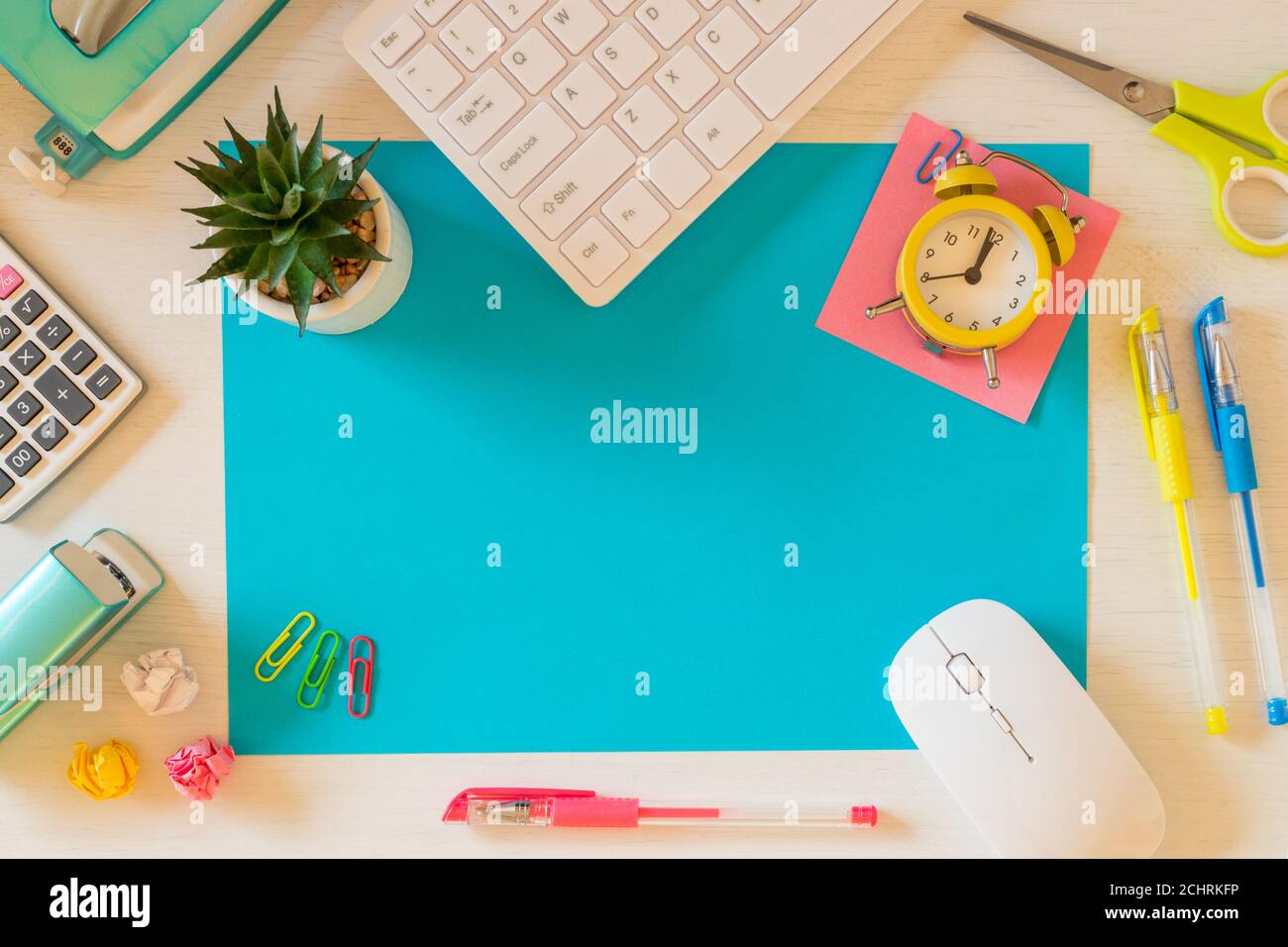 Una grande scheda blu vuota sulla scrivania con spazio per il testo. Accessori per ufficio e scuola, tastiera per computer, sveglia, penne, palle di carta sbriciolati, s Foto Stock