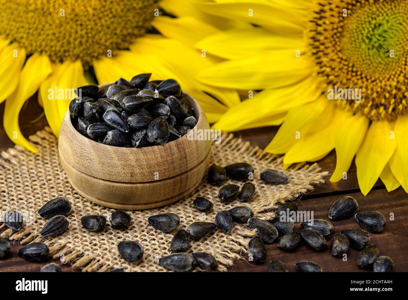 Semi di girasole in ciotola di legno e fiori di girasole sul tavolo marrone. Messa a fuoco selettiva. Foto Stock