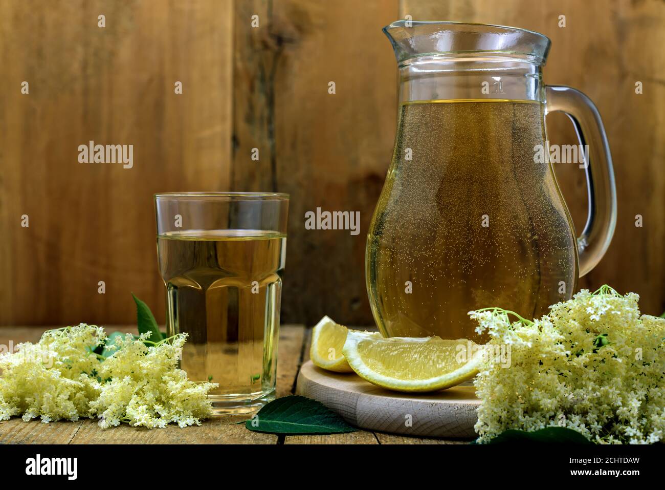 Un bicchiere e una caraffa di succo naturale di sambuco fatto in casa con fiori di limone e di anziano su vecchio tavolo di legno. Messa a fuoco selettiva. Foto Stock