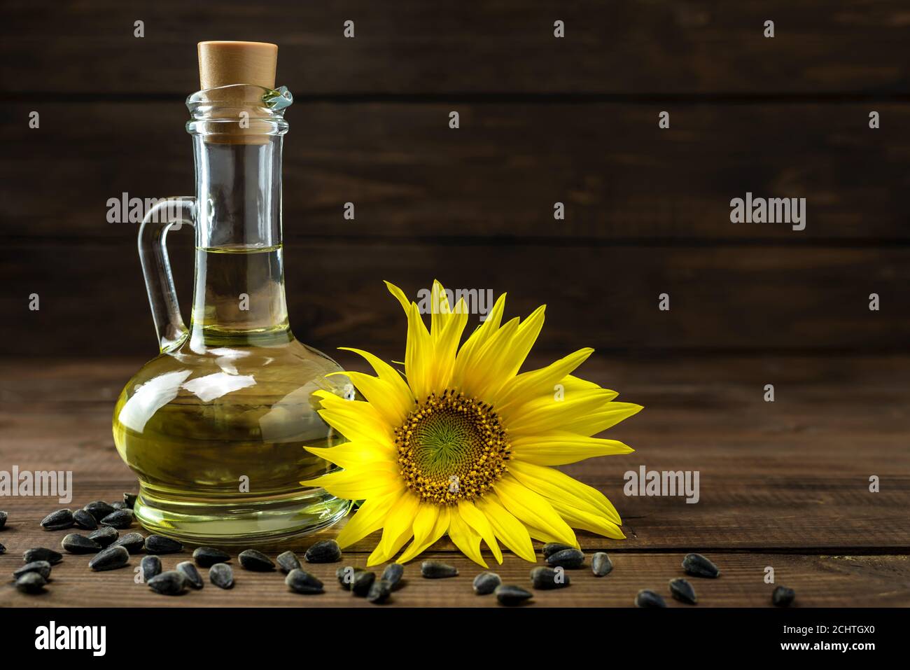 Olio di girasole in bottiglia e semi di girasole vicino a fiori di girasole freschi su sfondo di legno con spazio per la copia del testo. Foto Stock