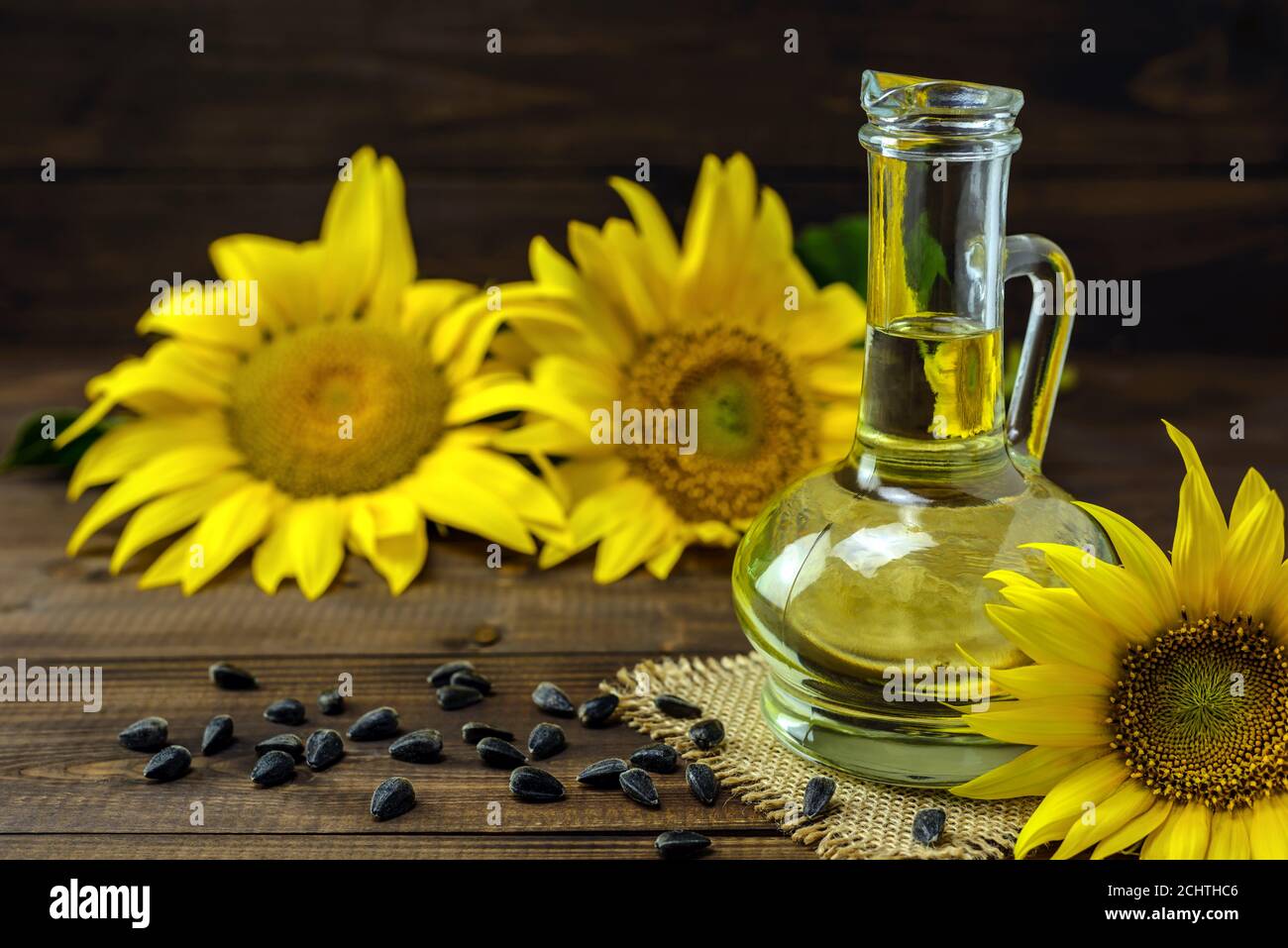 Olio di girasole in bottiglia e semi di girasole vicino a fiori di girasole freschi su sfondo di legno. Foto Stock