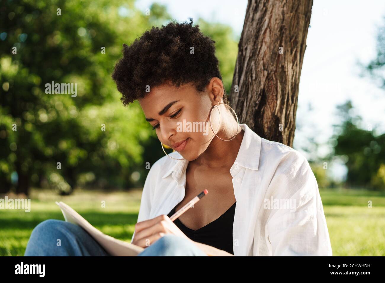 Foto di una donna africana concentrata seduta all'aperto nel parco un'erba mentre scrivono le note nel taccuino o nel diario Foto Stock