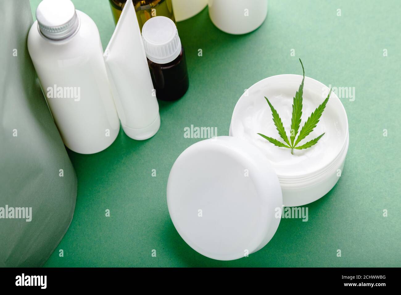 Crema idratante alla canapa in vaso bianco con cannabis a base di olio CBD foglie e set cosmetici per la cura della pelle su sfondo verde Foto Stock