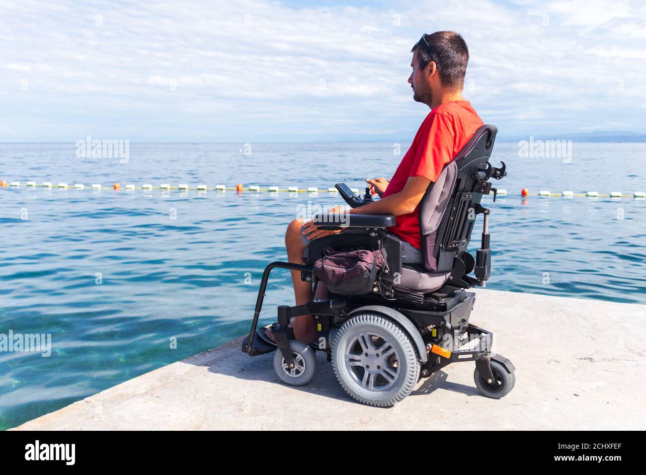 Uomo su sedia a rotelle che guarda l'oceano durante le vacanze estive. Foto Stock
