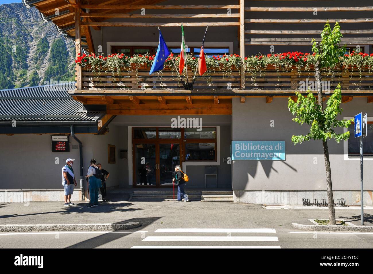 Facciata della biblioteca comunale con anziani con bastoni nordici per il nordic walking nella città di montagna ai piedi delle Alpi, Courmayeur, Aosta, Italia Foto Stock