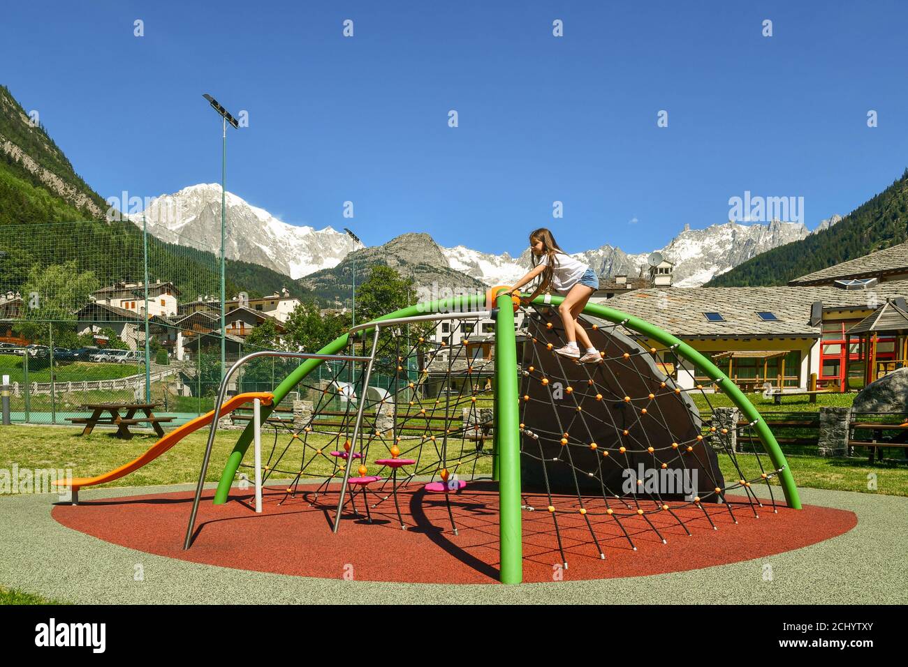 Bambina (10 anni) che arrampica una struttura di gioco in un parco giochi del villaggio alpino ai piedi del massiccio del Monte Bianco, Pré-Saint-Didier, Aosta, Italia Foto Stock