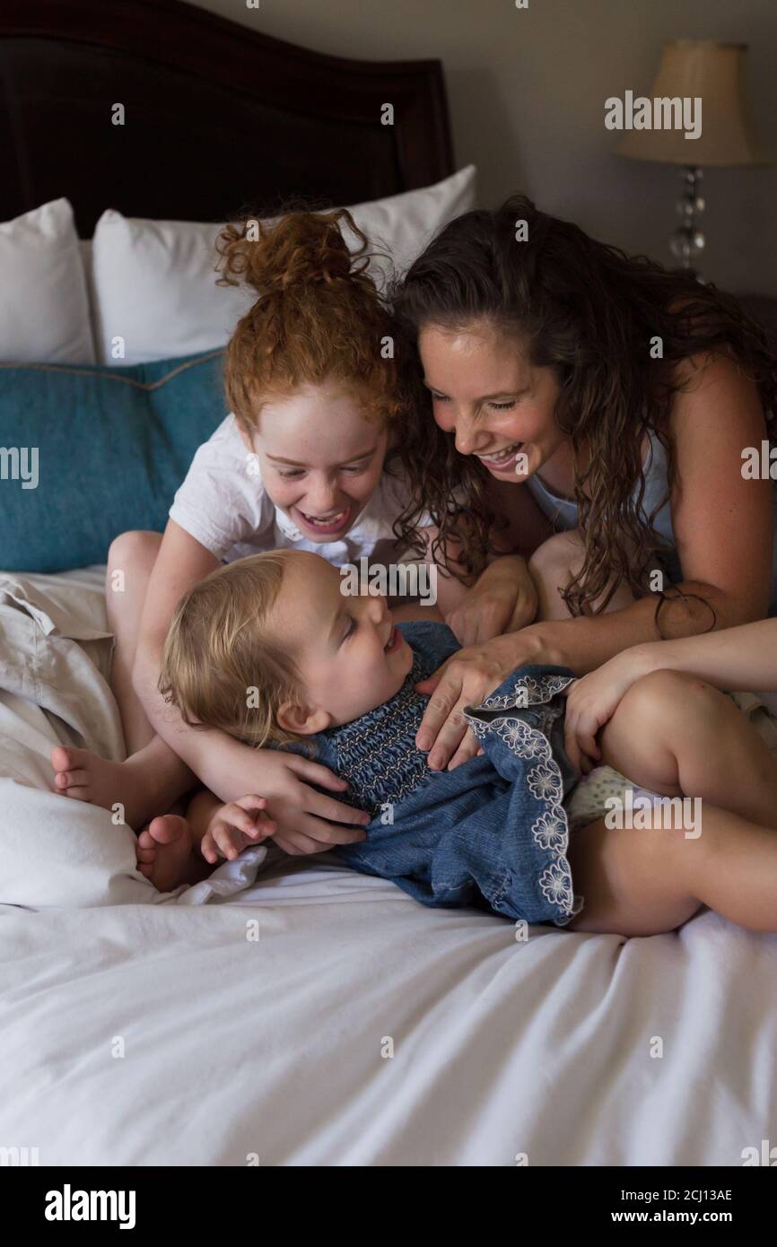 Madre e i bambini giovani si coccolano e giocano insieme su un Letto Foto Stock