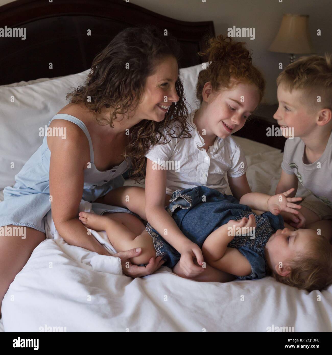 Madre e i bambini giovani si coccolano e giocano insieme su un Letto Foto Stock