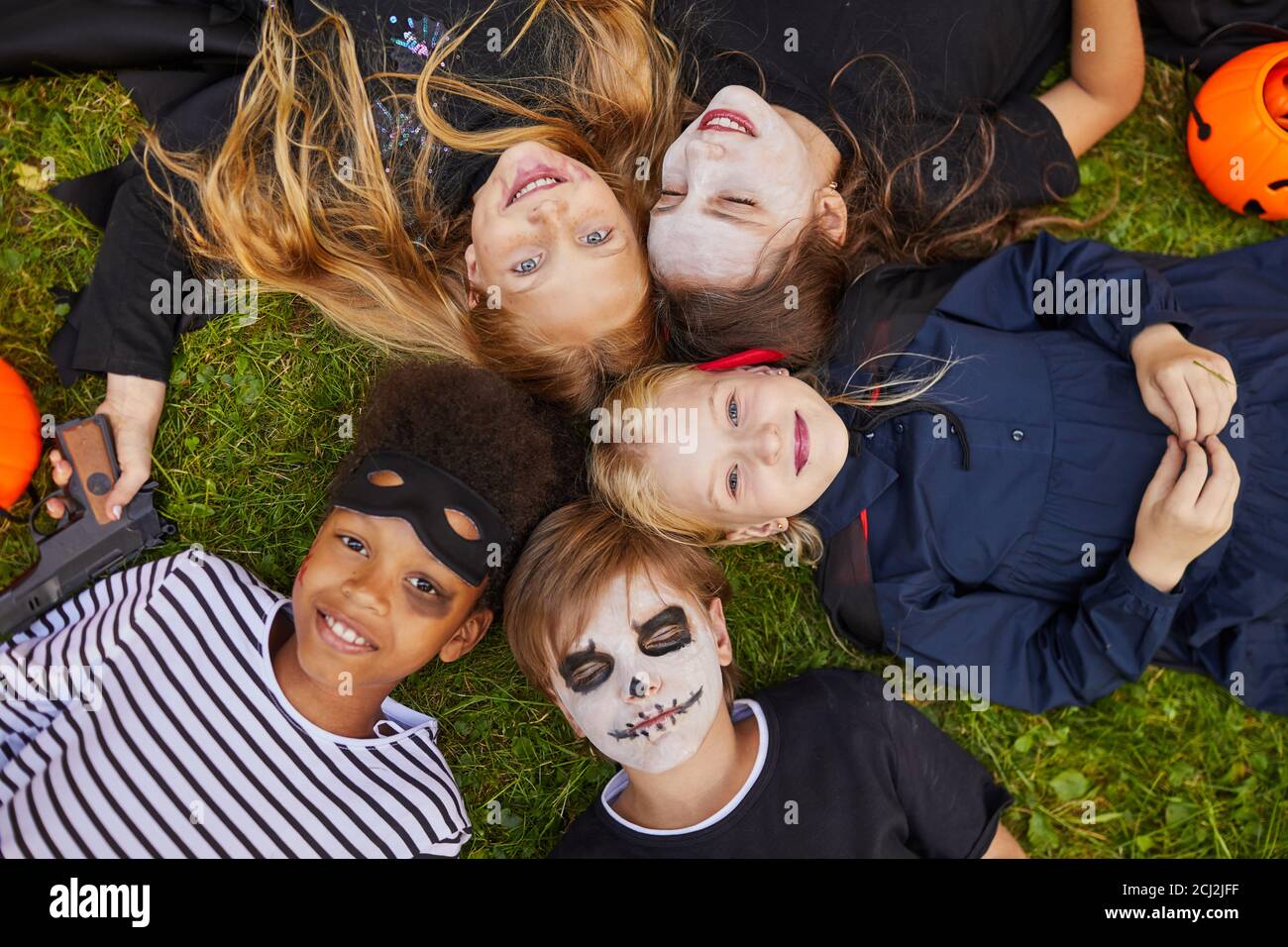 Vista dall'alto su un gruppo multietnico di bambini che indossano costumi di Halloween mentre giace sull'erba e guardando la macchina fotografica Foto Stock