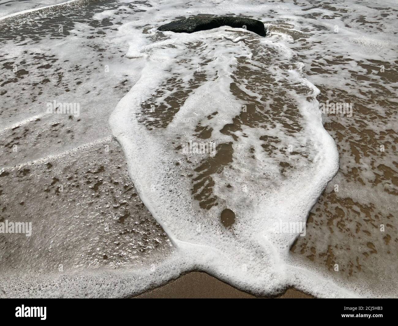 Marea oceanica, sabbia, schiuma e roccia. Foto Stock