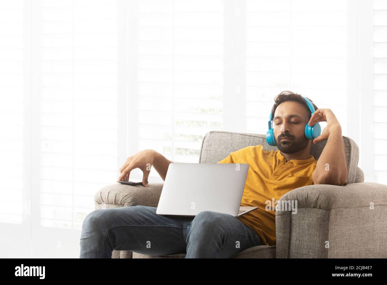 Giovane che ascolta musica e si rilassa sul divano con un laptop in grembo Foto Stock