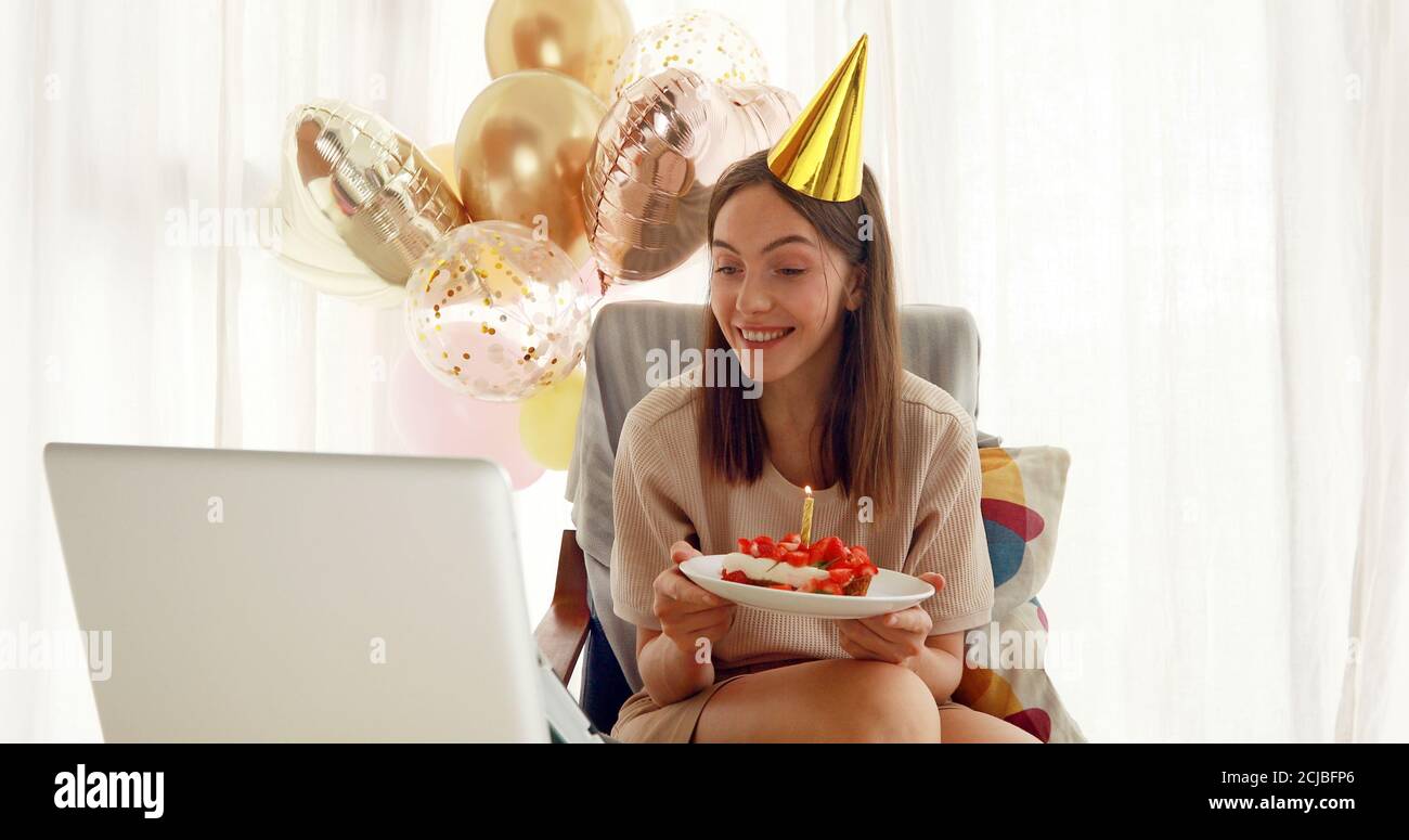 La donna soffia la candela sulla torta davanti al computer portatile Foto Stock