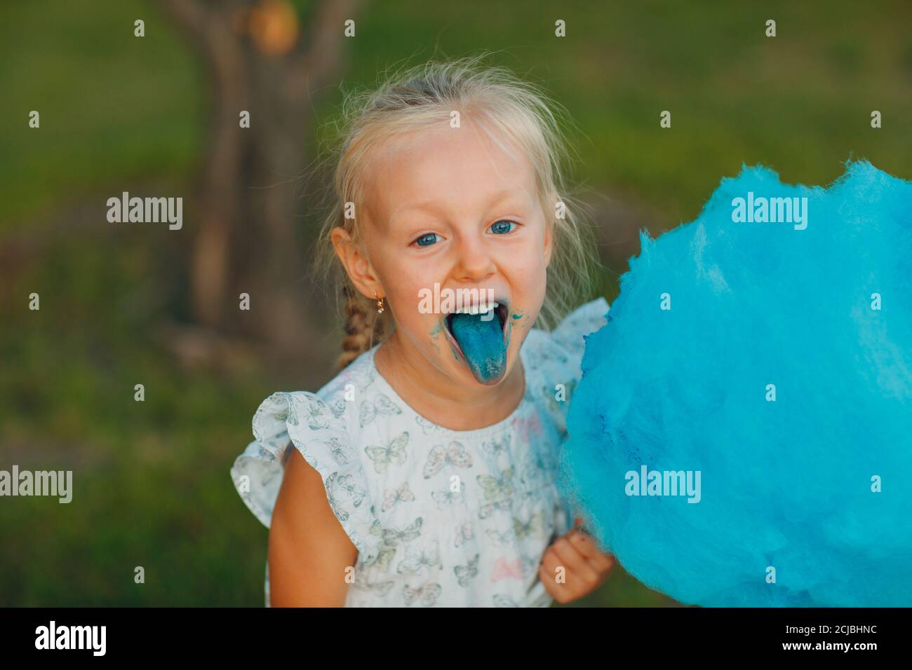 Bambina bionda che mangia caramelle di cotone e mostra la lingua blu nel  parco Foto stock - Alamy