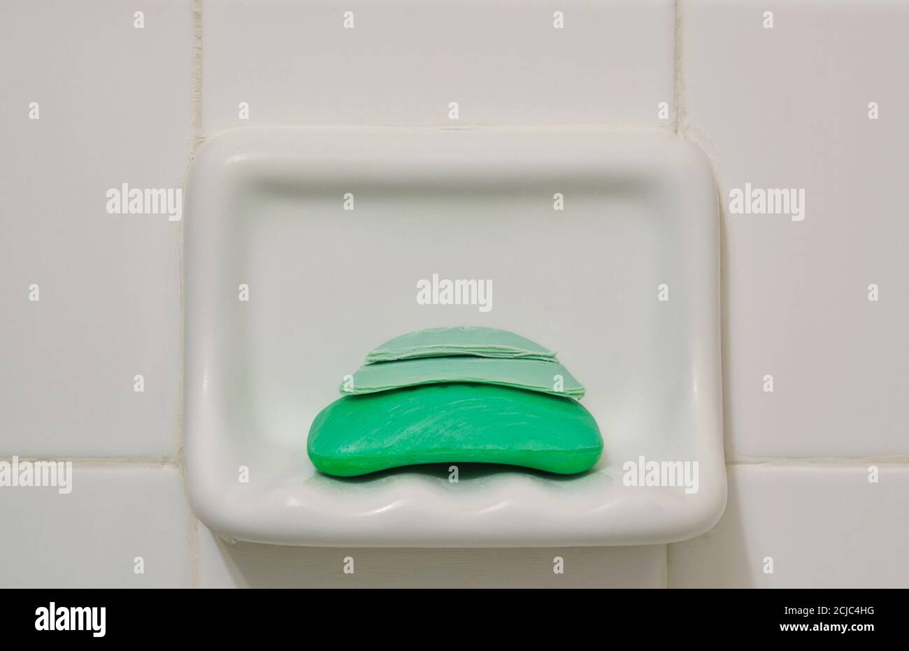 Vecchie barre di sapone di scarto attaccate ad una nuova in un supporto della doccia della stanza da bagno e sfondo bianco della piastrella. Concetto di riciclaggio dei rifiuti. Foto Stock