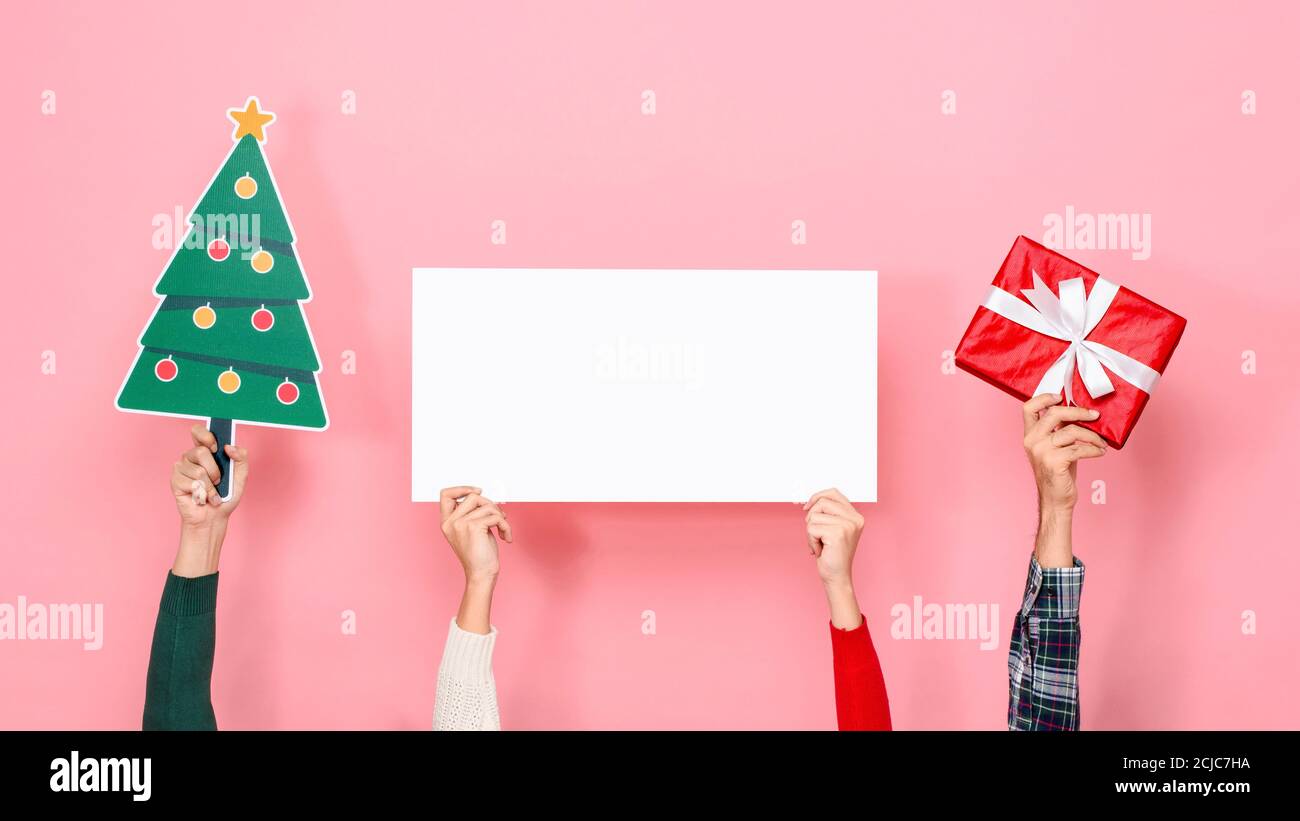 Mani che tengono scatola regalo, albero di Natale e cartoncino bianco con spazio vuoto per il testo su sfondo rosa isolato Foto Stock