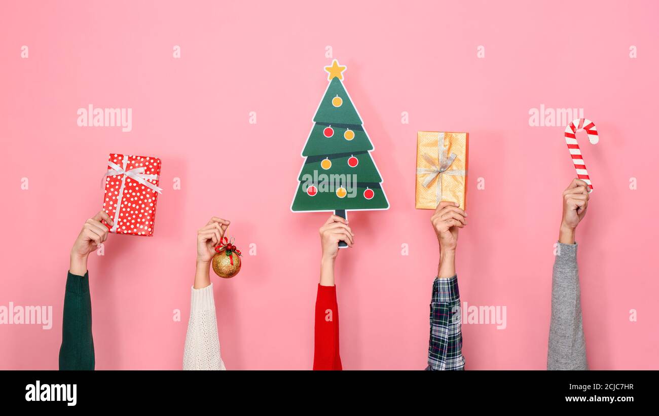 Mani che tengono le scatole di regalo e gli articoli decorativi di Natale colorati sopra sfondo rosa isolato Foto Stock