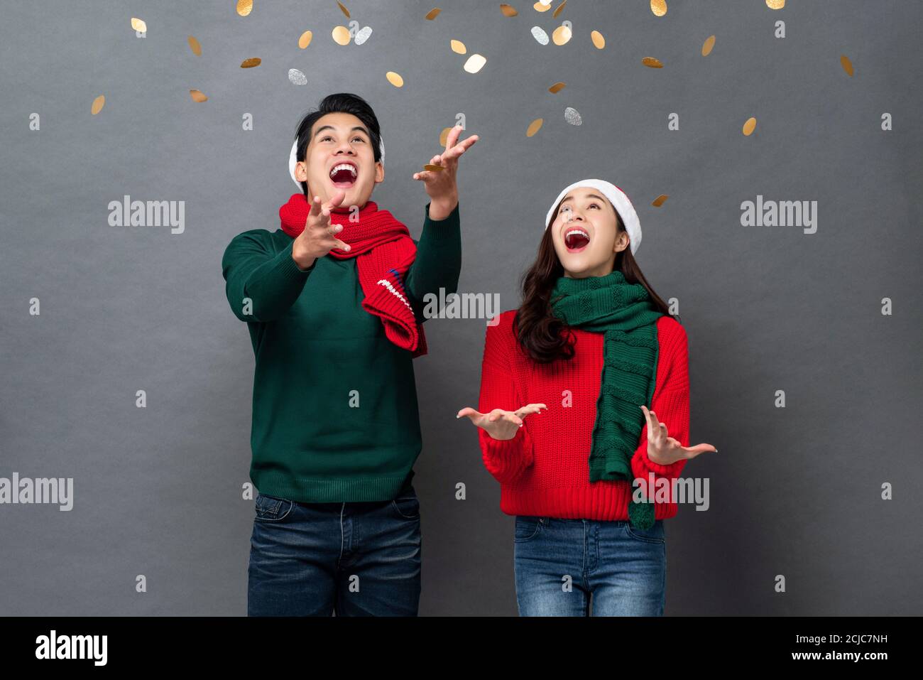 Eccitata coppia asiatica in abbigliamento natalizio giocando con confetti in sfondo grigio studio Foto Stock