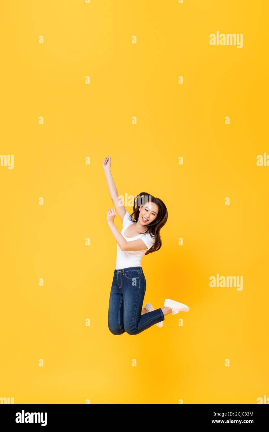 Ritratto a lunghezza intera di bella donna asiatica sorridente e saltando a mezz'aria isolata su sfondo giallo con spazio di copia in alto Foto Stock