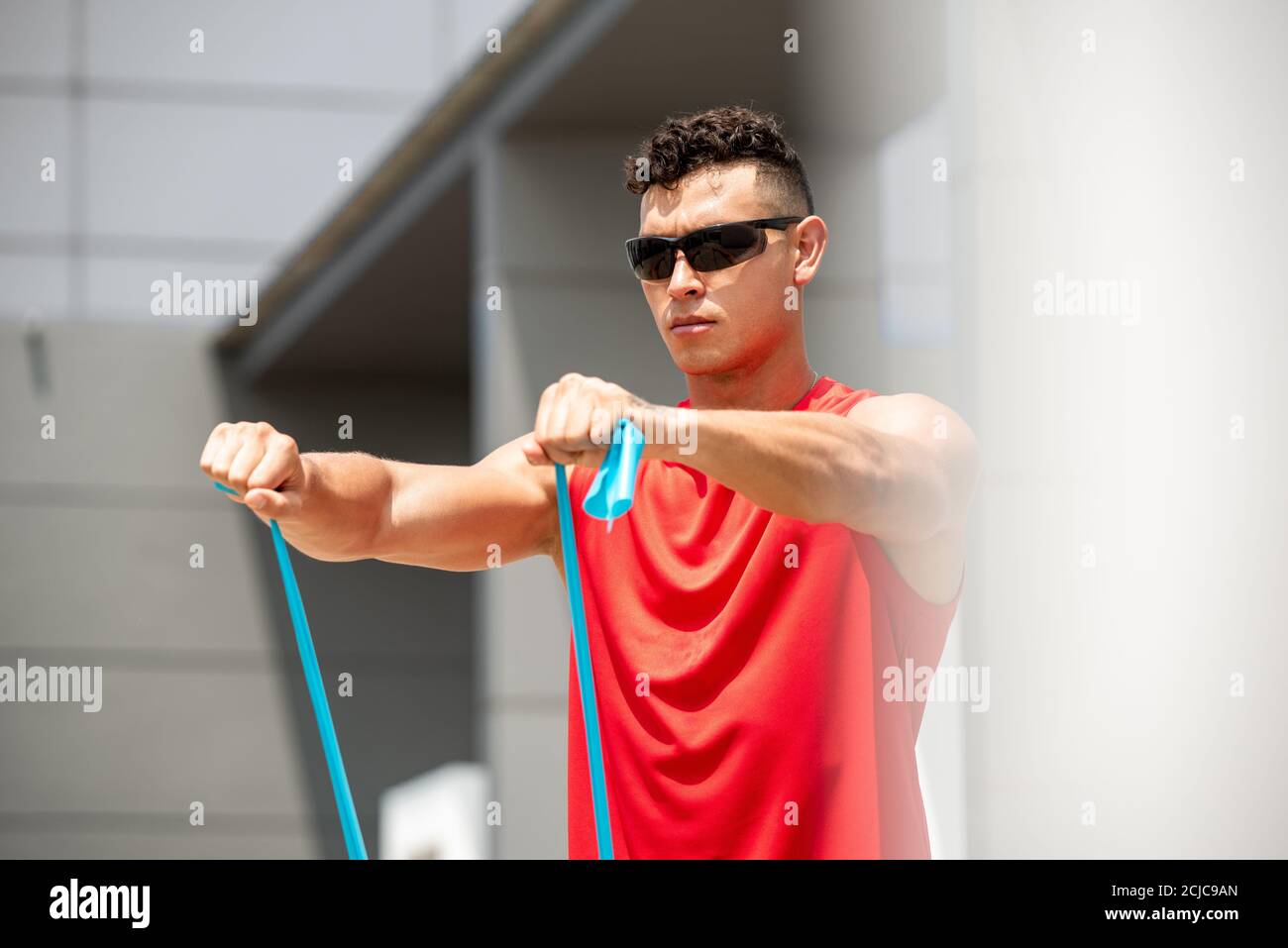 Bell'uomo sportivo che fa fronte a spalla solleva l'esercizio con resistenza band all'aperto al sole Foto Stock