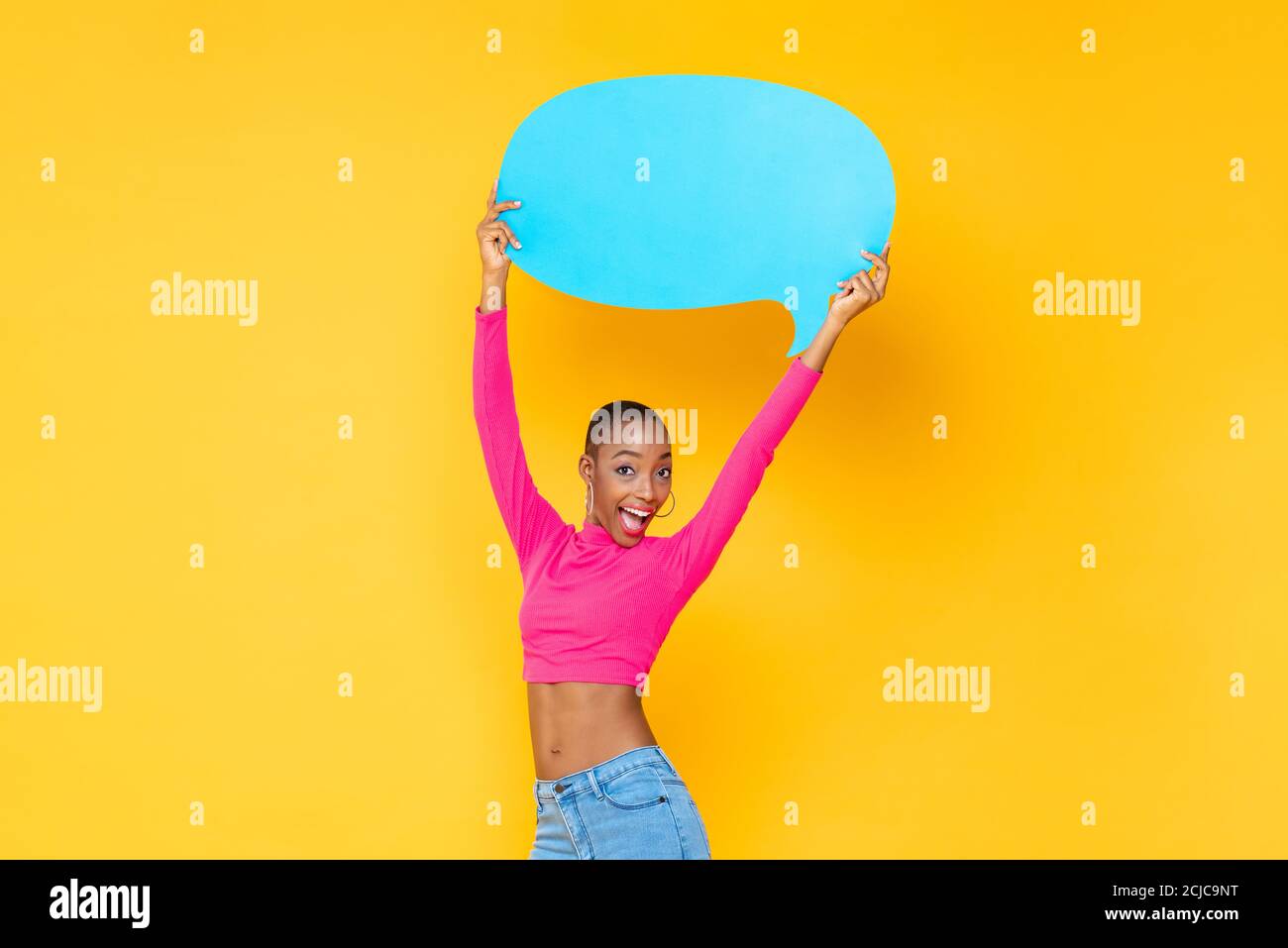 Bella donna afro-americana eccitata sorridente e sollevante discorso vuoto bolla isolato su colorato sfondo giallo studio Foto Stock