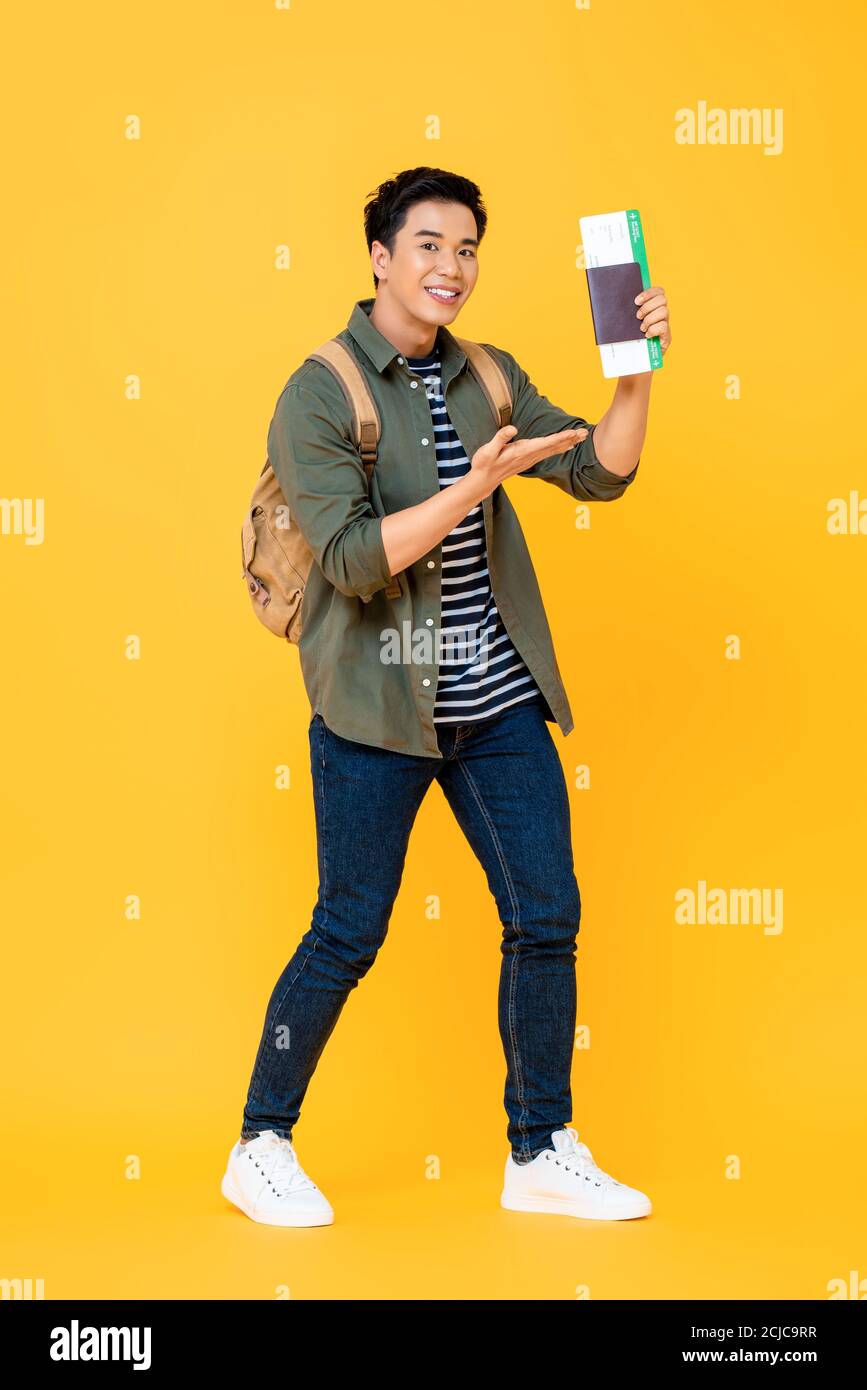 Ritratto a lunghezza intera di eccitato giovane asiatico zaino in spalla turista uomo con passaporto e carta d'imbarco isolati su sfondo giallo dello studio Foto Stock